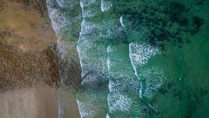 Aerial view features a Massachusetts coastline with soft waves crashing on the sand. 