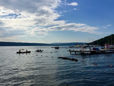 A view from the edge of a dock looking out to a lake filled with a few boats and another jutting dock with a few people on it. Blue sky is in the background.
