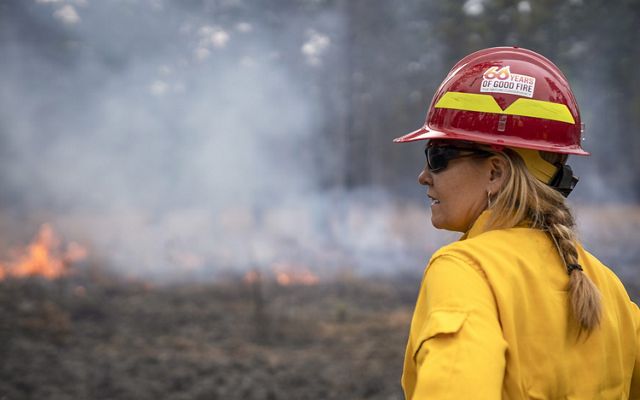 Candid photo of TNC CEO Jennifer Morris dressed in fire-protective gear and hard hat watching a controlled burn at Piney Grove Preserve.