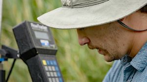 Close-up of a researcher's face in the foreground, and an out-of-focus scientific instrument in the background.