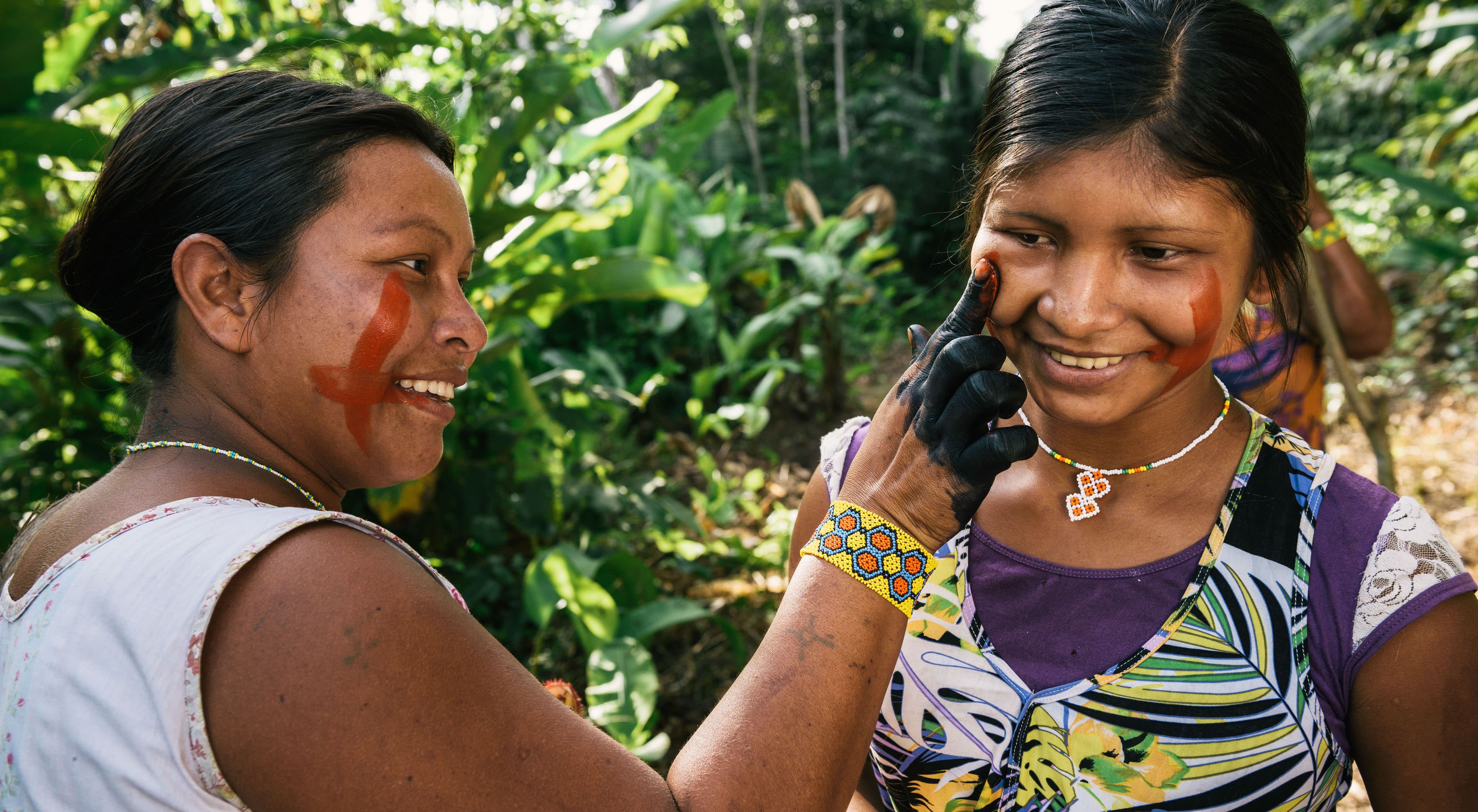 Xikrin women painting each other's faces in a forest near the Pot-Kro Village, Brazil.