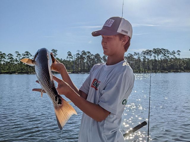Young man holds up a redfish to examine it as he stands on a boat in the Pensacola Blackwater Bay.