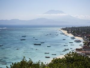 an expansive view of an Indonesian island's coastline with fishing boats and a tall mountain on the horizon