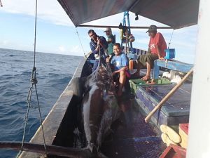 Several men sit on the deck of a small boat with a large fish on the deck.