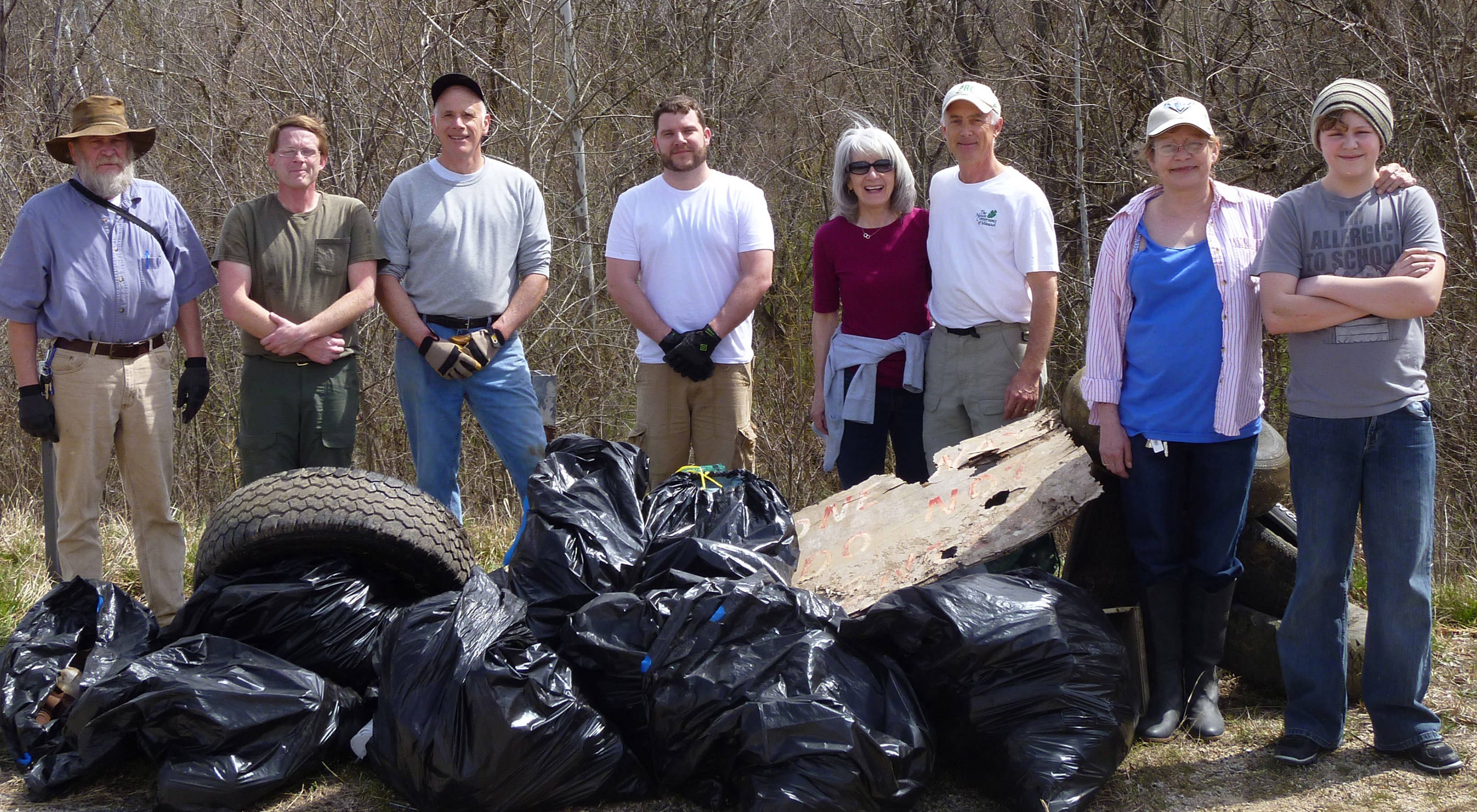 A group of smiling volunteers stand with the trash they've removed during a cleanup day.