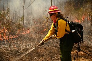 Dressed in fire-protective gear, Zoe McGee uses a hose to spray a fire line during a controlled burn.