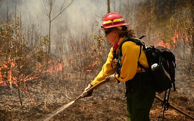 Dressed in fire-protective gear, Zoe McGee uses a hose to spray a fire line during a controlled burn.